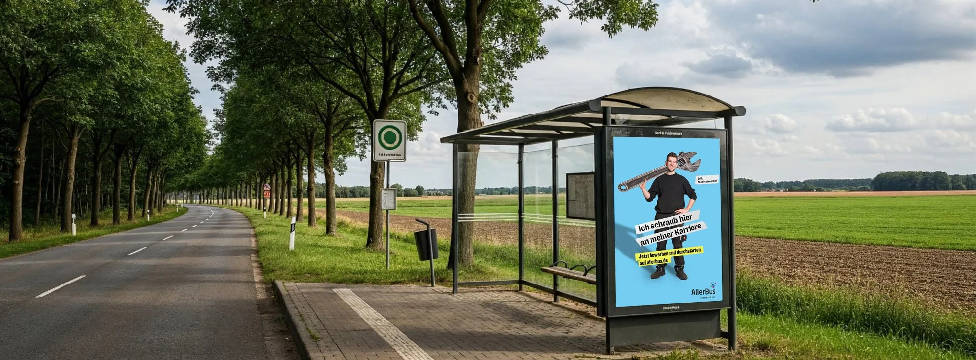 Bushaltestelle an einer Landstraße zwischen Feldern, im Werbekasten ein Motiv der Aller-Bus-Kampagne